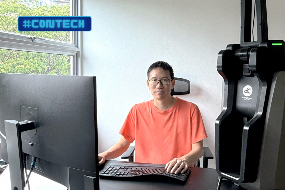 Engineer seated at desk using computer beside 3D scanning equipment.